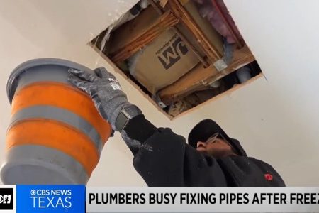 Plumber repairing frozen pipes indoors, using a bucket to catch water, highlighting urgent plumbing services during freezing temperatures.